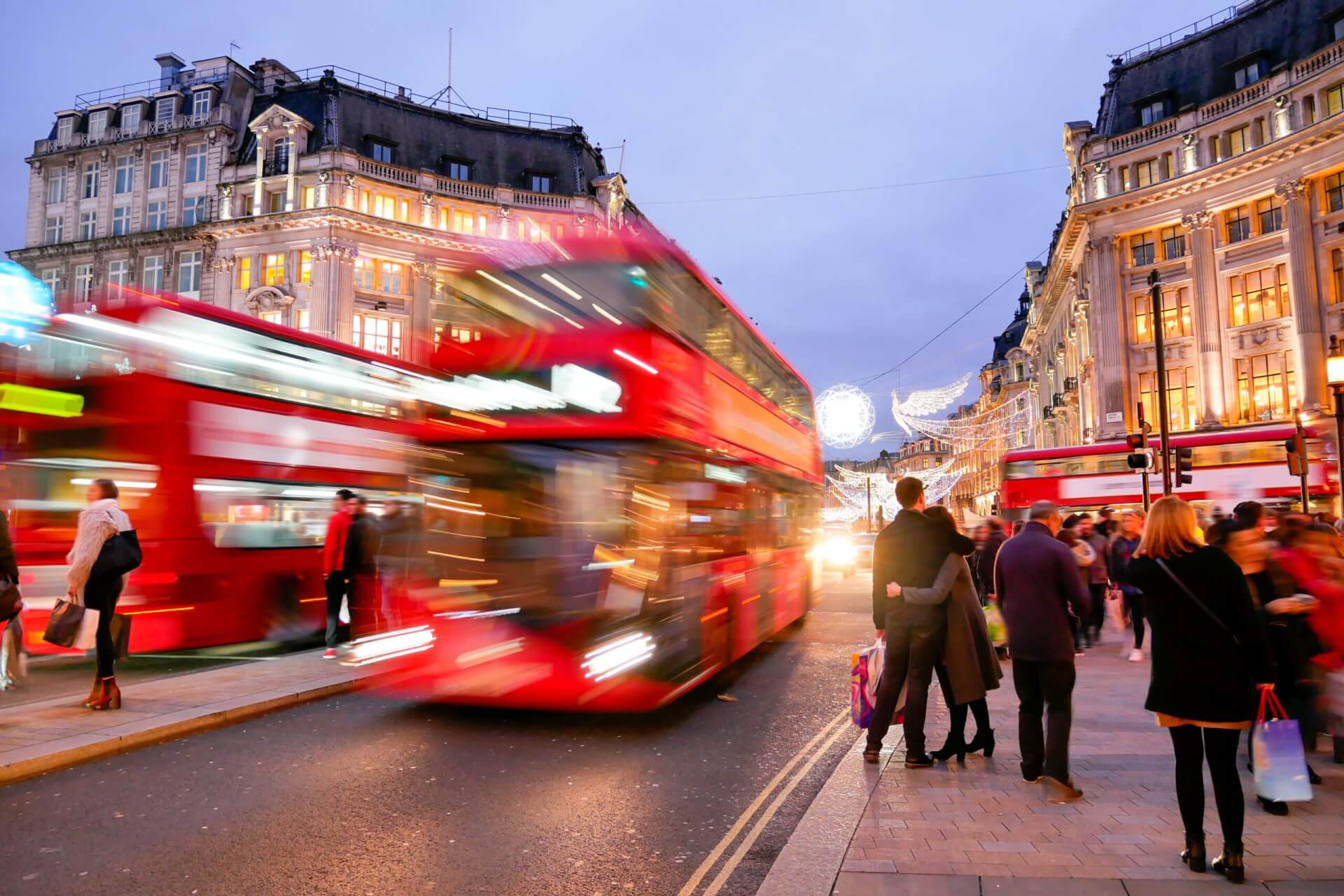 London's West End with a blurred red bus driving down Regent Street at dusk with lots of shoppers on the pavements