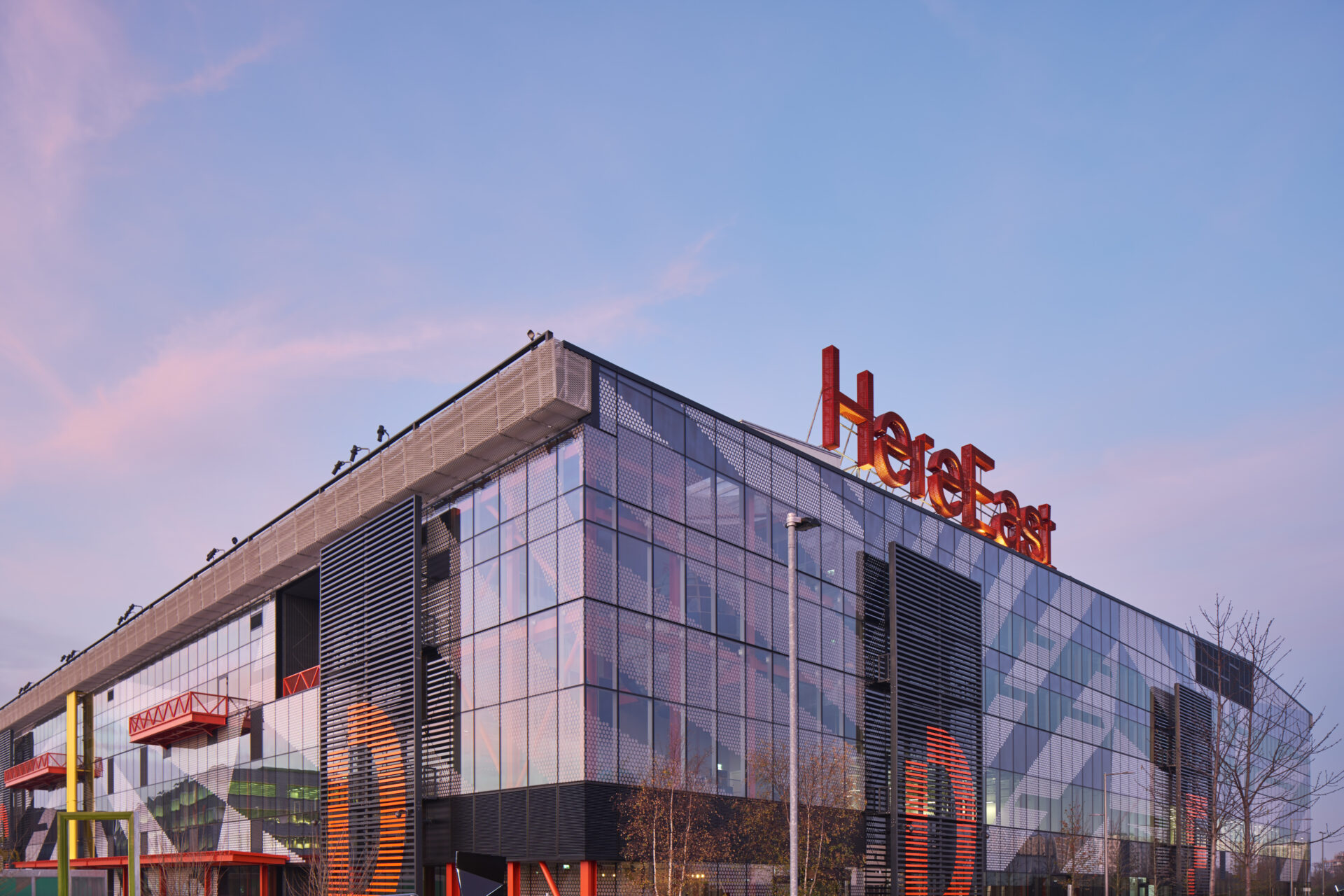 A modern office building featuring lots of external glazing with a large red Here East sign on top
