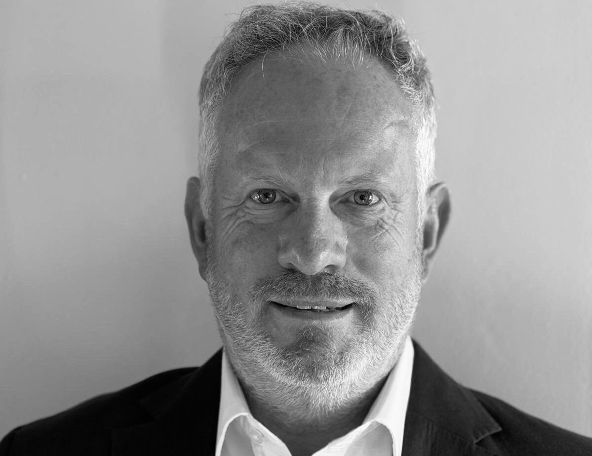 Black and white picture of Ivan Scott who is wearing a dark suit, a white shirt and no tie