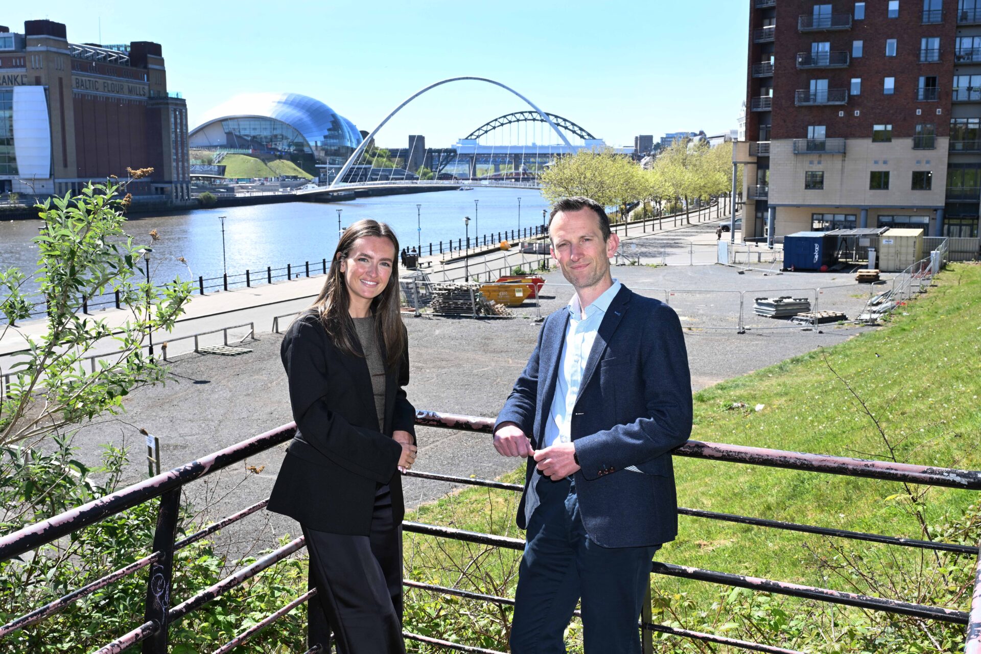 A white female stood to the left and a white male wearing a suit stood on Newcastle's Quayside
