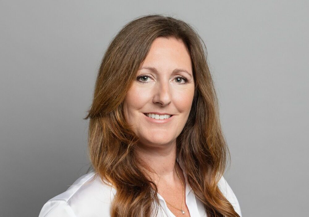 A middle-aged woman with long brown hair wearing a white satin shirt