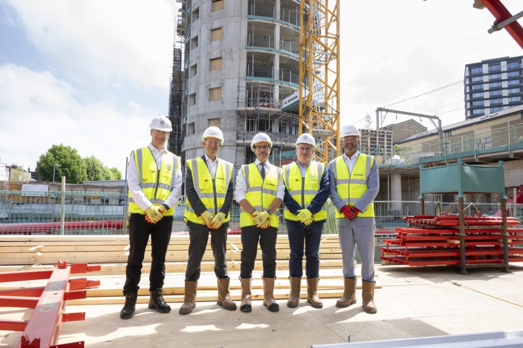 Five men wearing high vis jackets and hard hats stood on a building site