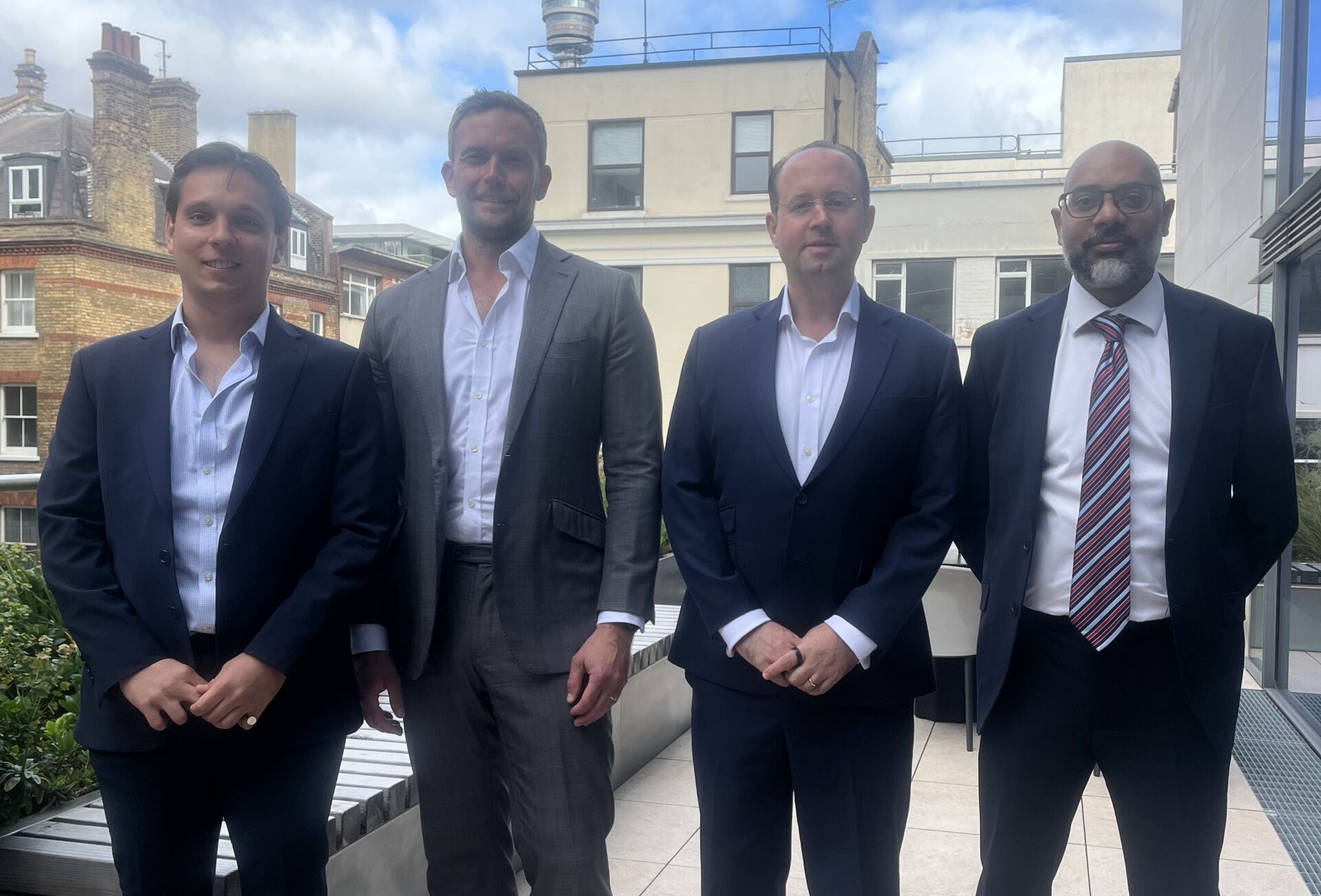 Four men stood side by side wearing suits