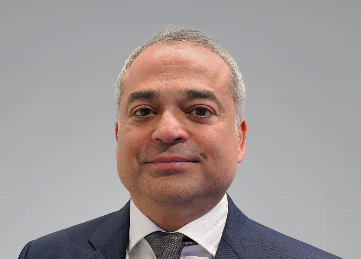 A smiling man with short grey hair wearing a blue suit jacket and a white shirt with a tie