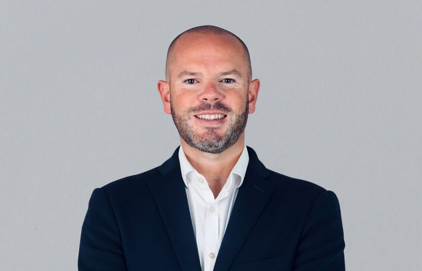 A smiling man wearing a dark suit jacket and a white shirt