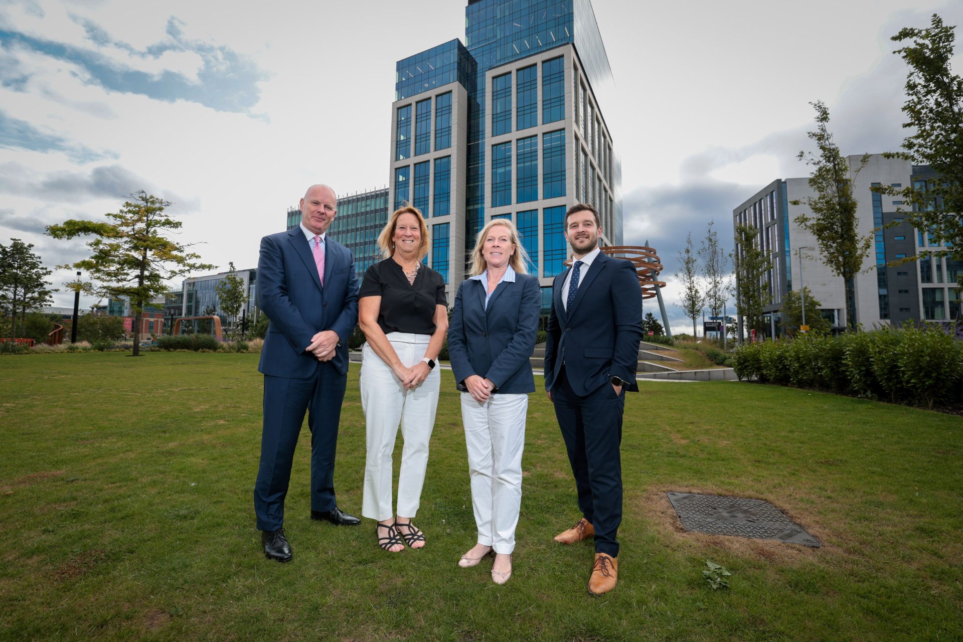 Two men and two women stood on a green lawn in front of a large office building