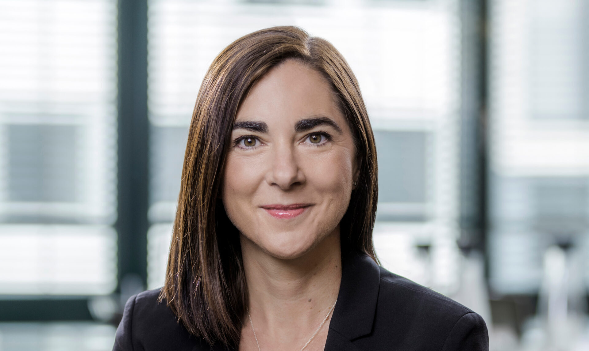 A smiling woman with long brown hair wearing a dark jacket
