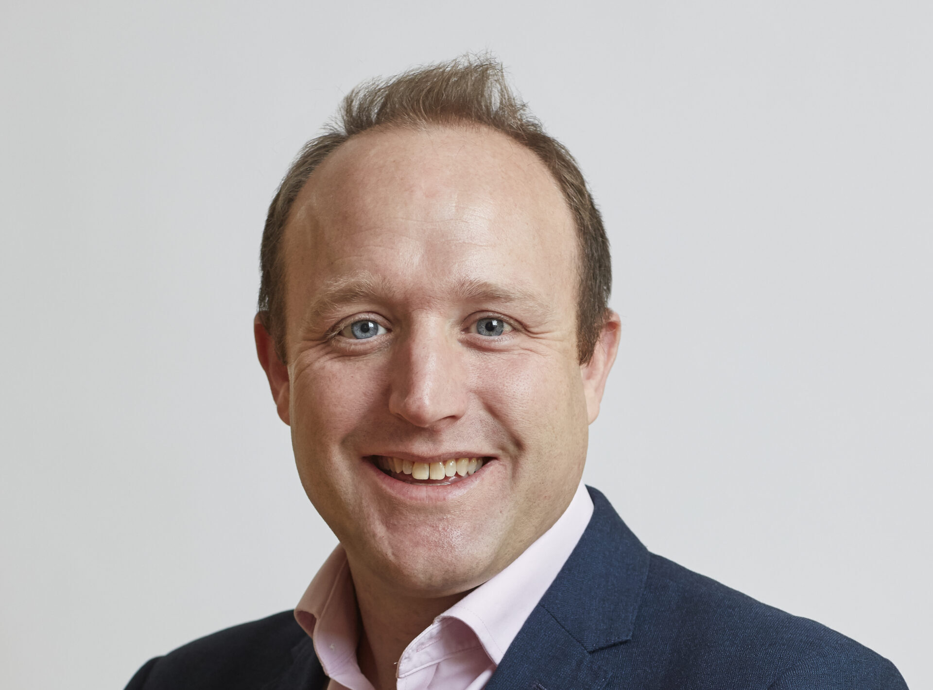 A smiling man wearing a dark suit jacket and a light coloured shirt