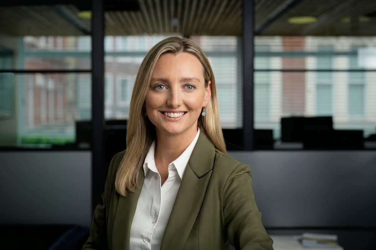 A smiling woman with long brown hair wearing a green jacket and a white shirt