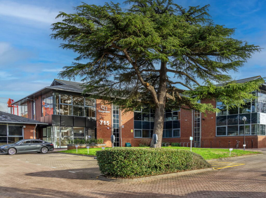 A brick built office building with a large tree and hedge in front