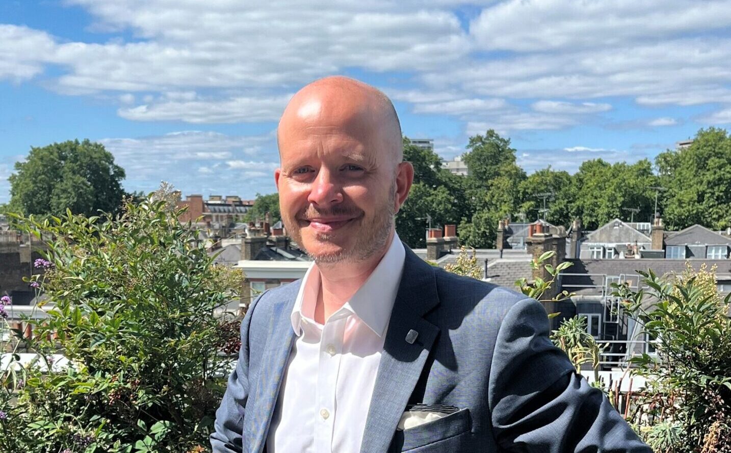 A man wearing a suit with greenery in the background