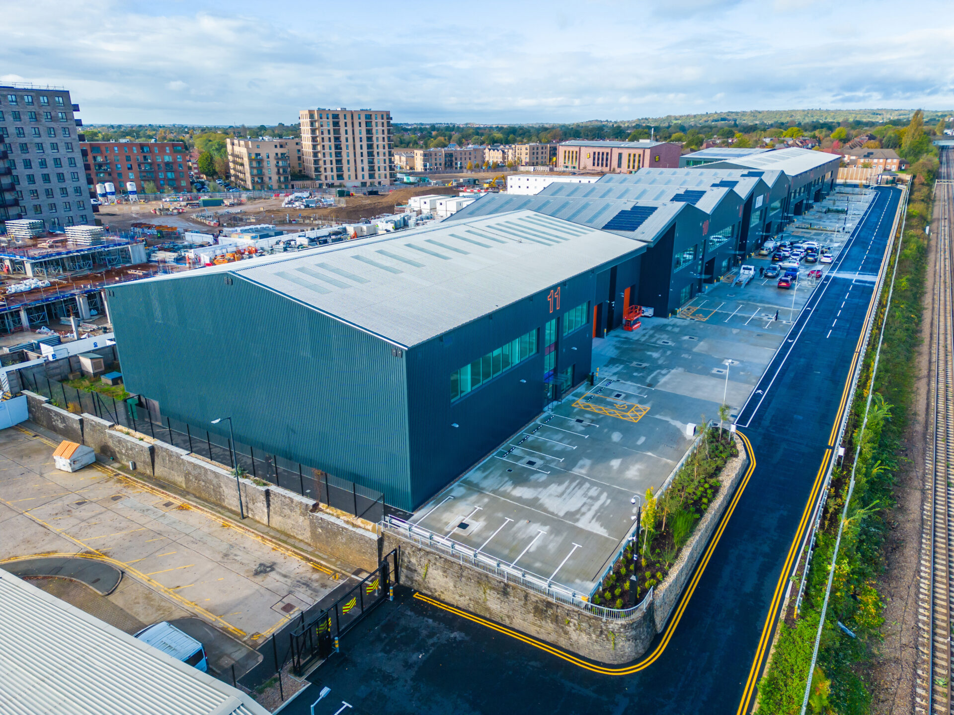 Aerial view of a row of blue industrial buildings with a development site in the background
