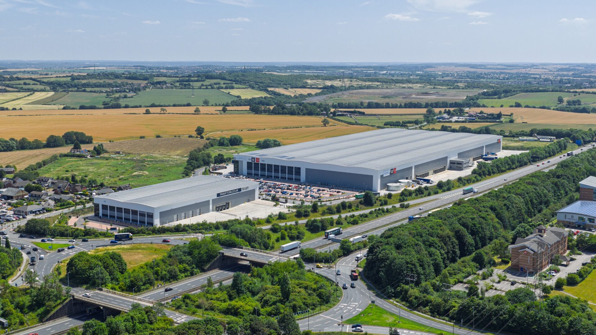 Aerial view of two large industrial buildings surrounded by roads and fields