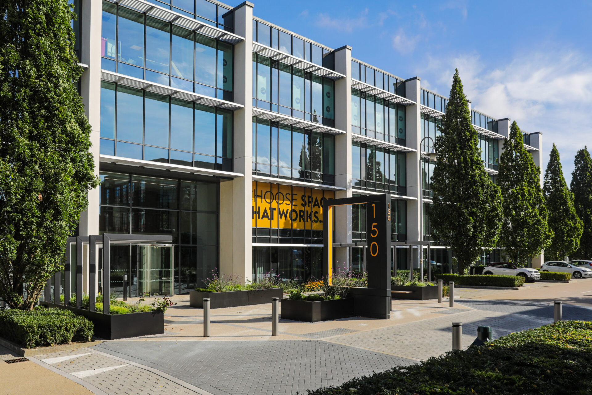 Exterior of a modern low-rise office building featuring lots of glass windows along the facade with trees and landscaping in the foreground