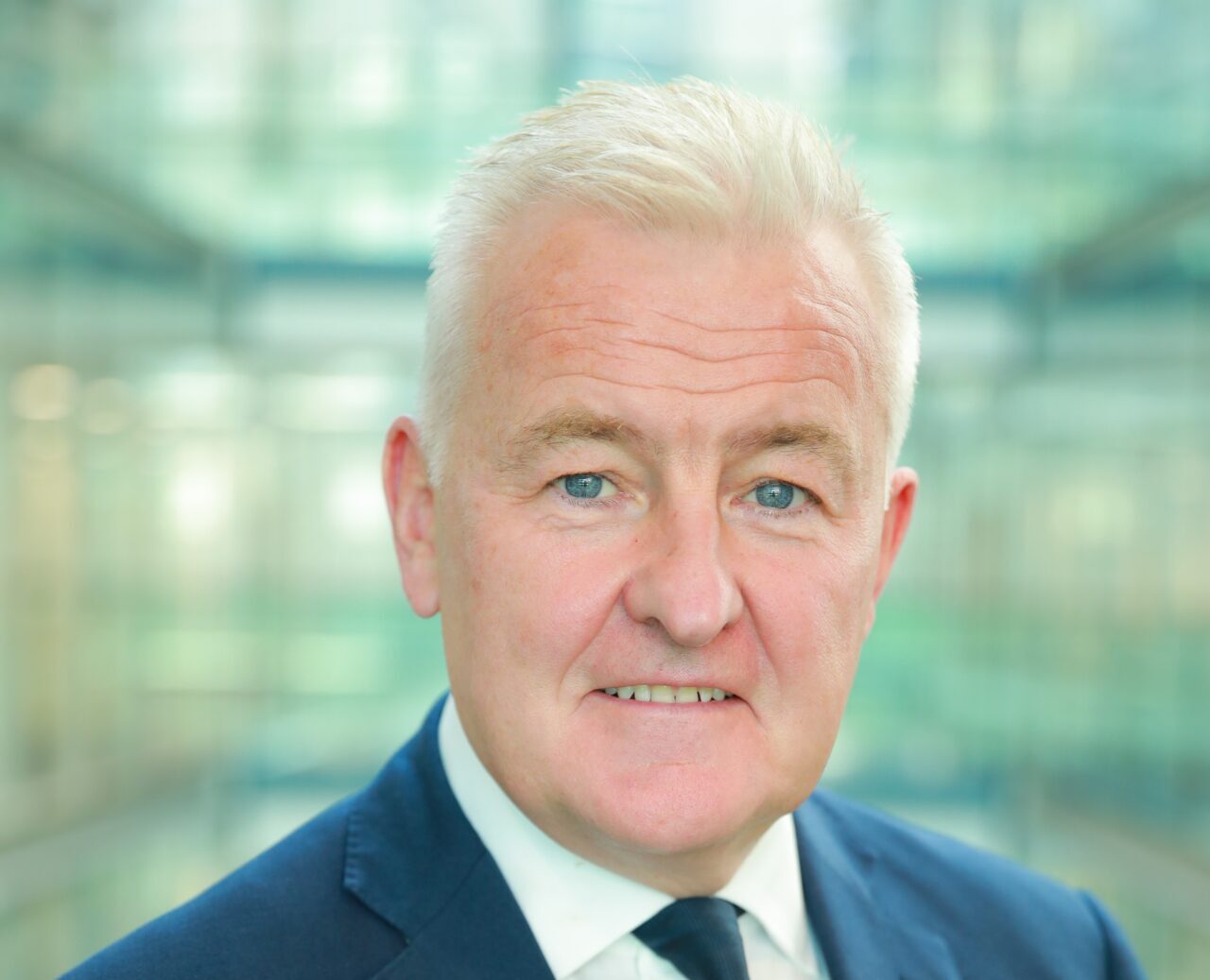 A grey haired man wearing a dark blue suit and tie and a white shirt