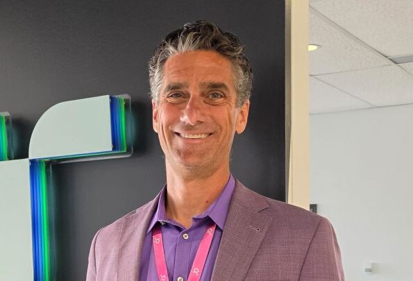 Man wearing a purple shirt and jacket stood next to a company logo