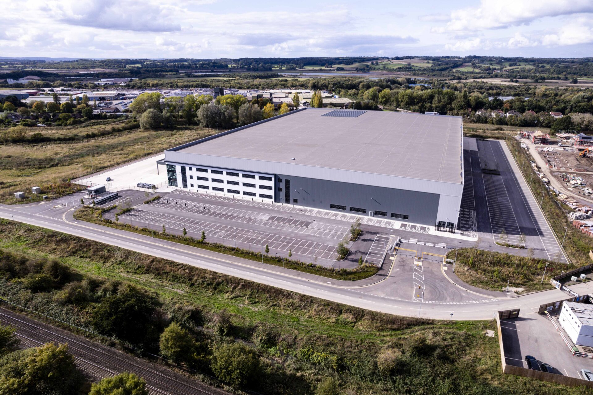 Aerial view of a large modern industrial building surrounded by a wooded area and grassland