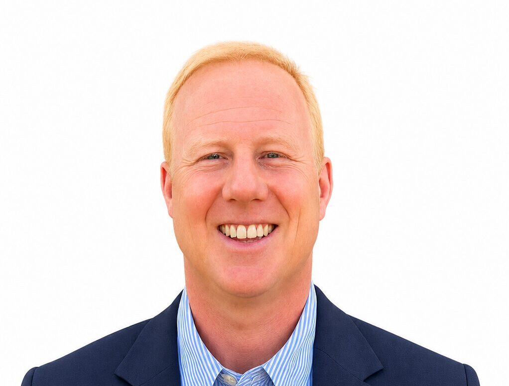 A smiling man wearing a dark suit jacket and a light blue pin-striped shirt