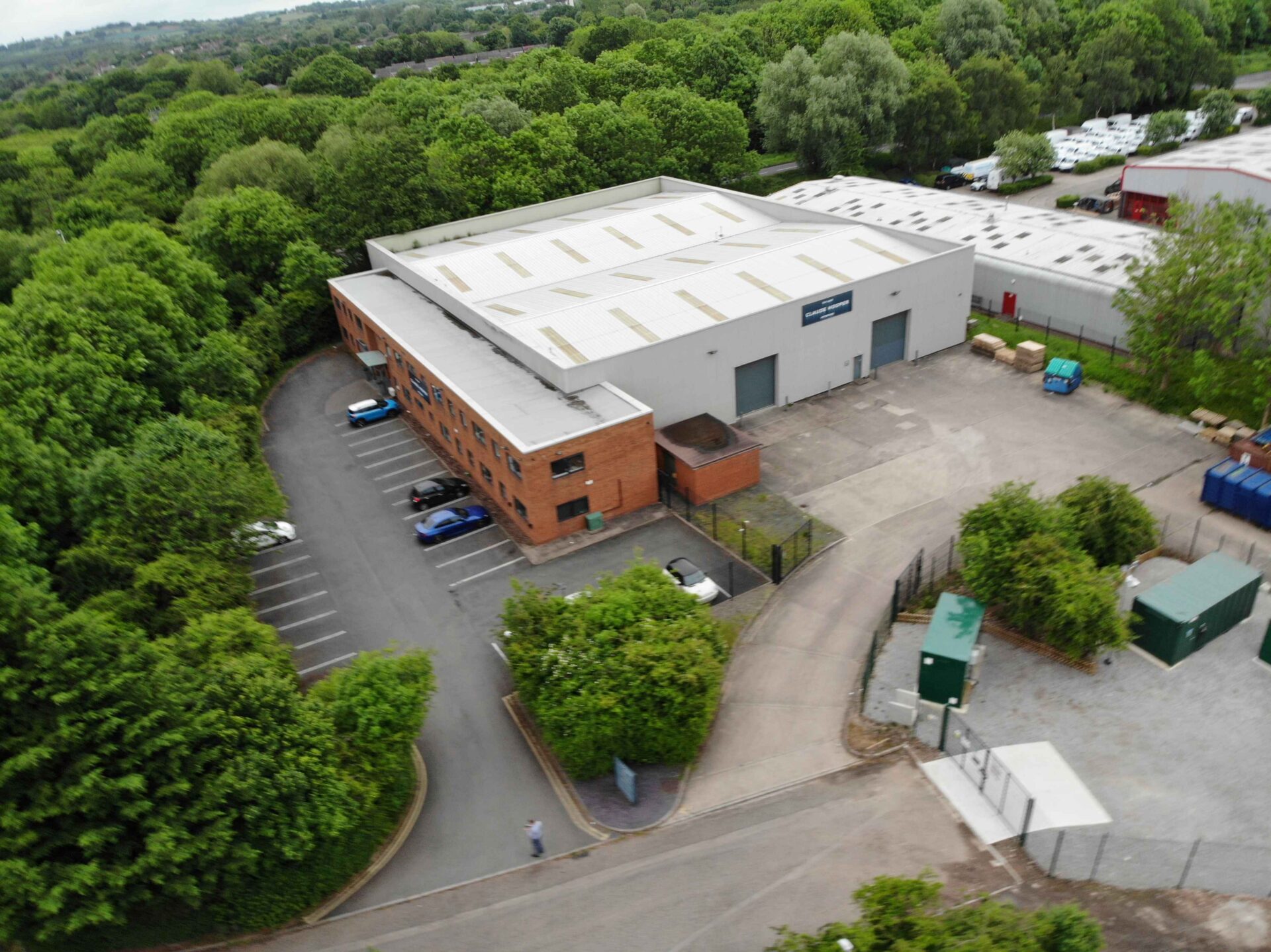 Aerial view of an industrial building with a large wooded area to the side and the rear