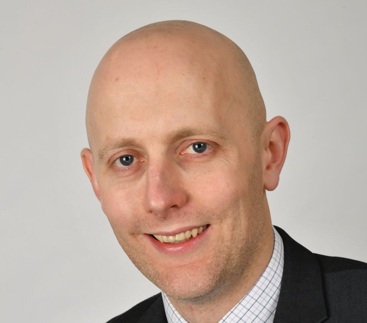 A smiling bald man wearing a suit jacket and collared shirt