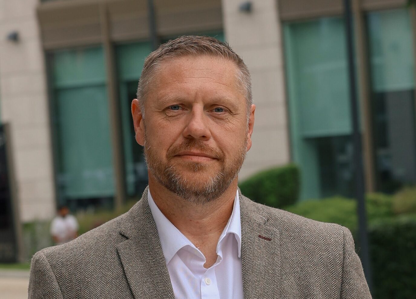 A white male with a short beard and short hair wearing a jacket and white shirt