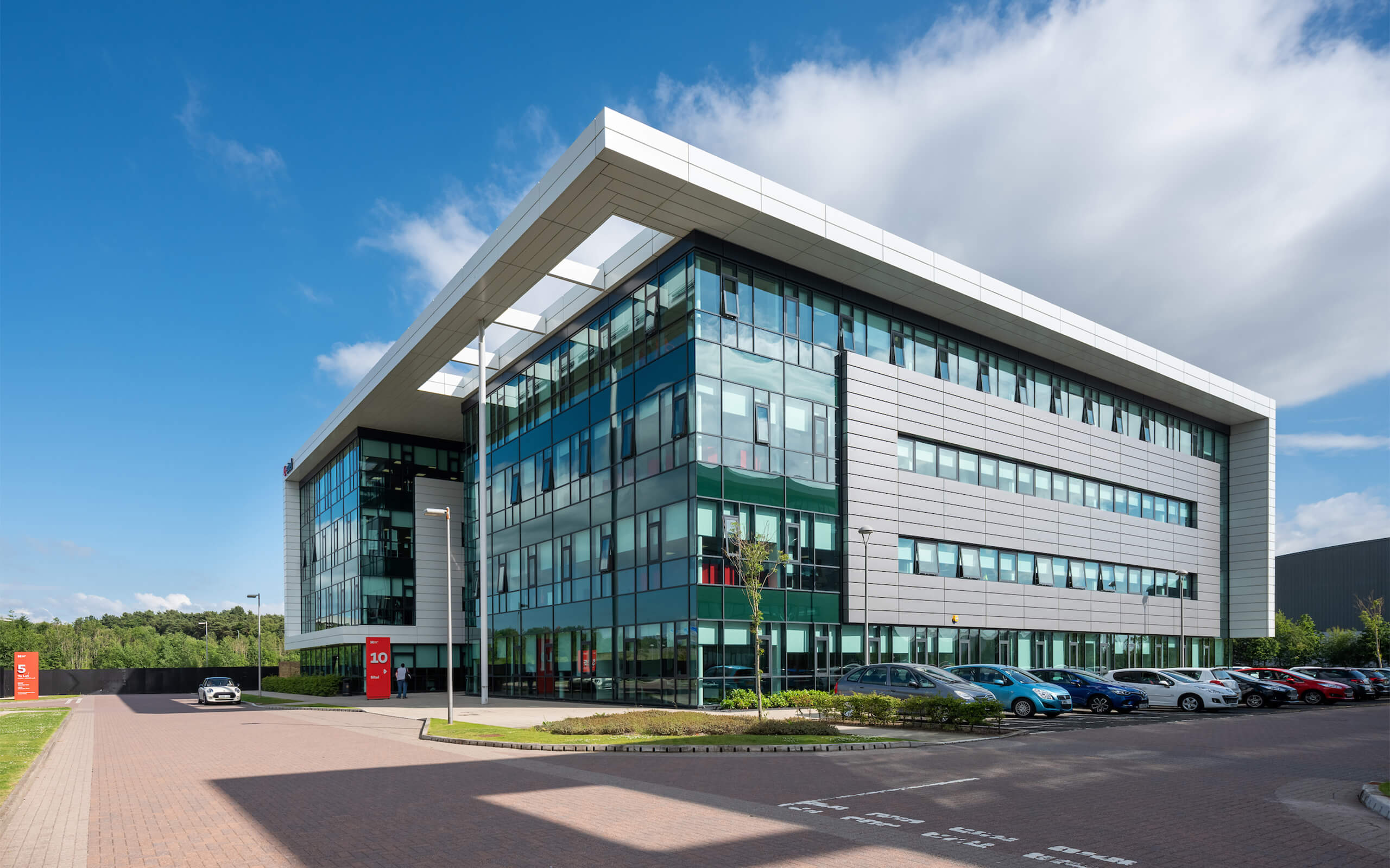 A modern office building featuring lots of glazing and cladding on its facade with car parking to the front