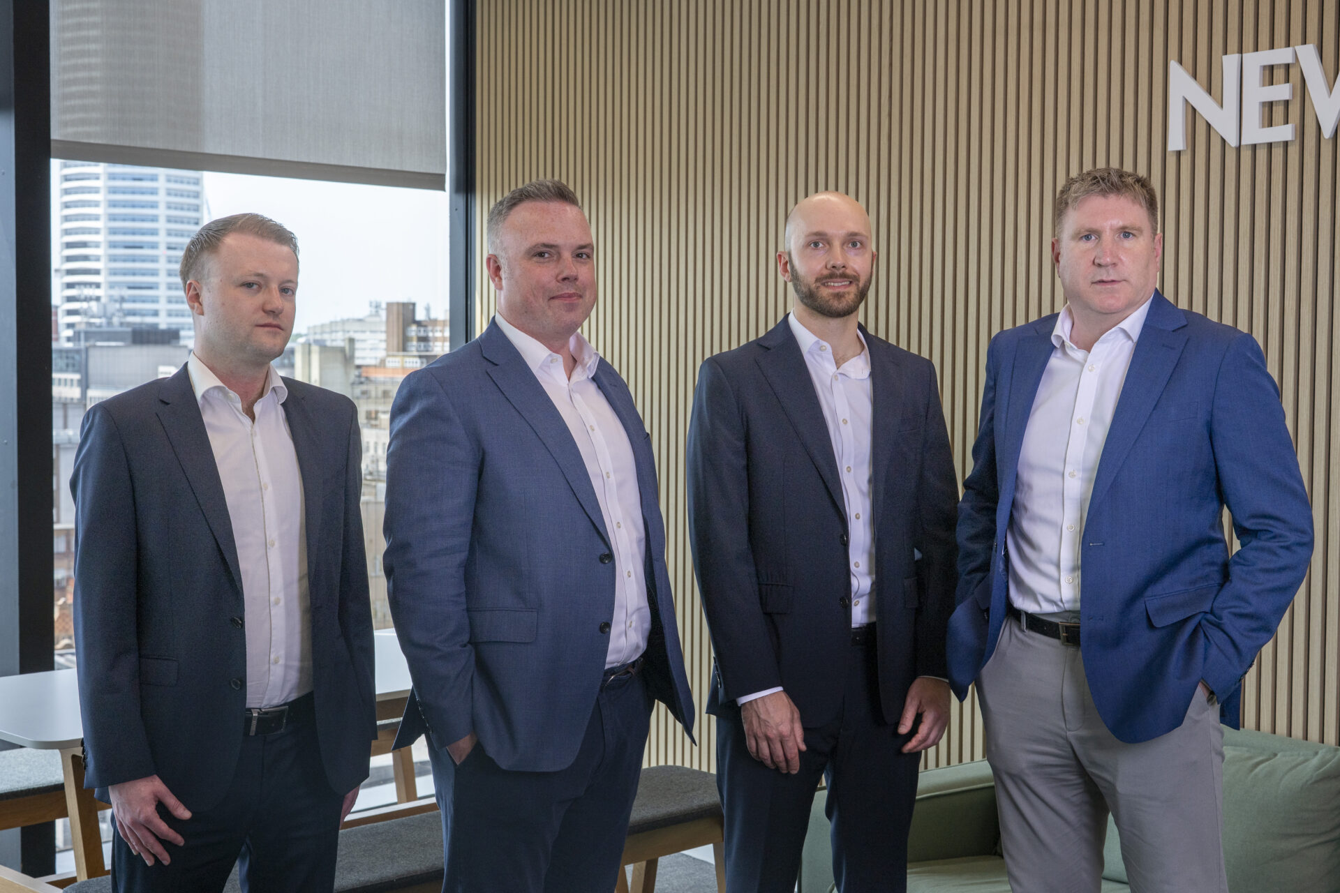 Four white males wearing suits stood in an office