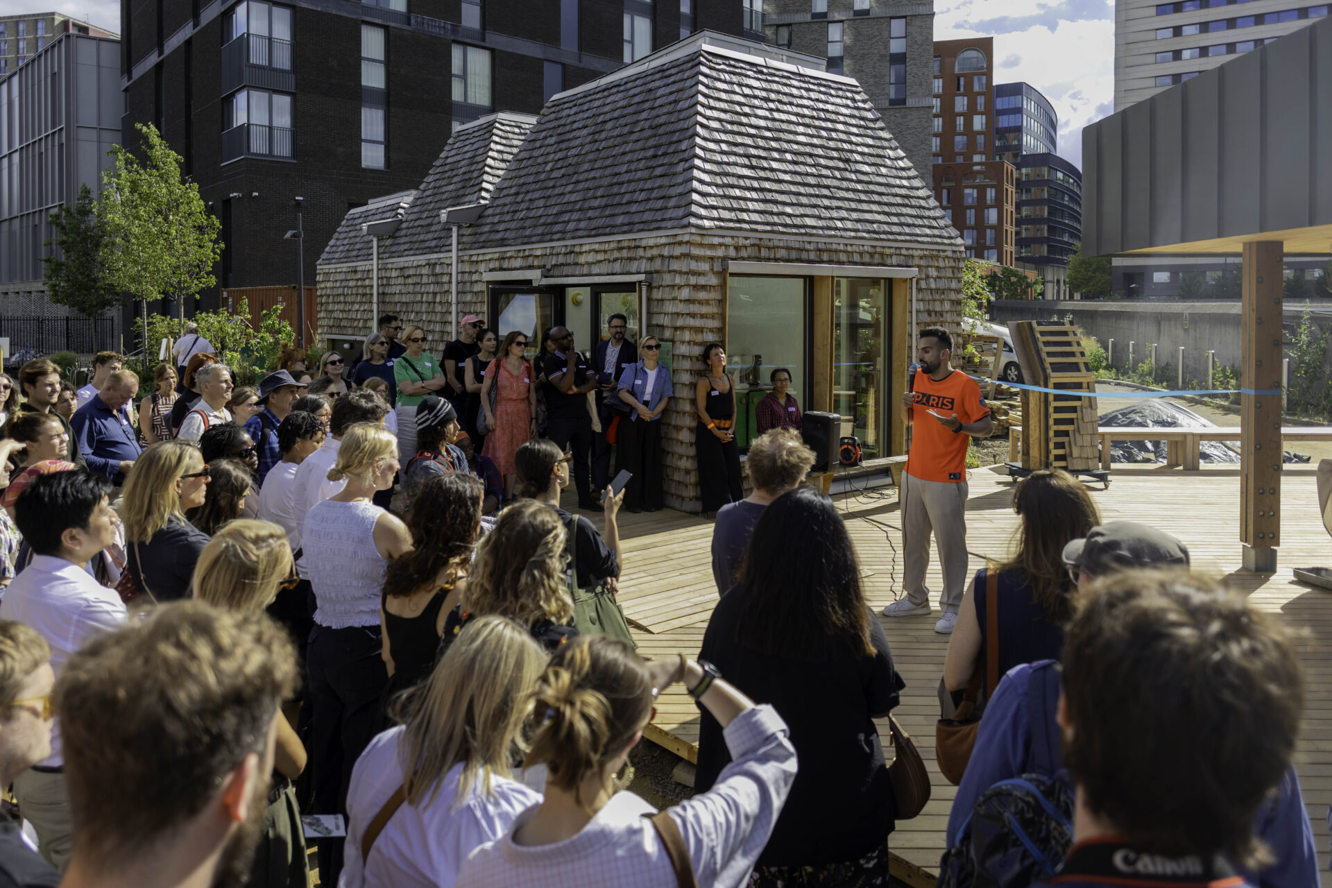 A man wearing a bright shirt stood in front of a crowd of people at a new neighbourhood garden at King's Cross