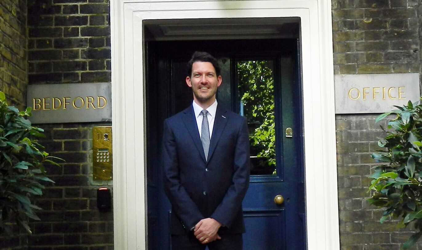 A man wearing a dark suit stood in front of an ornate doorway