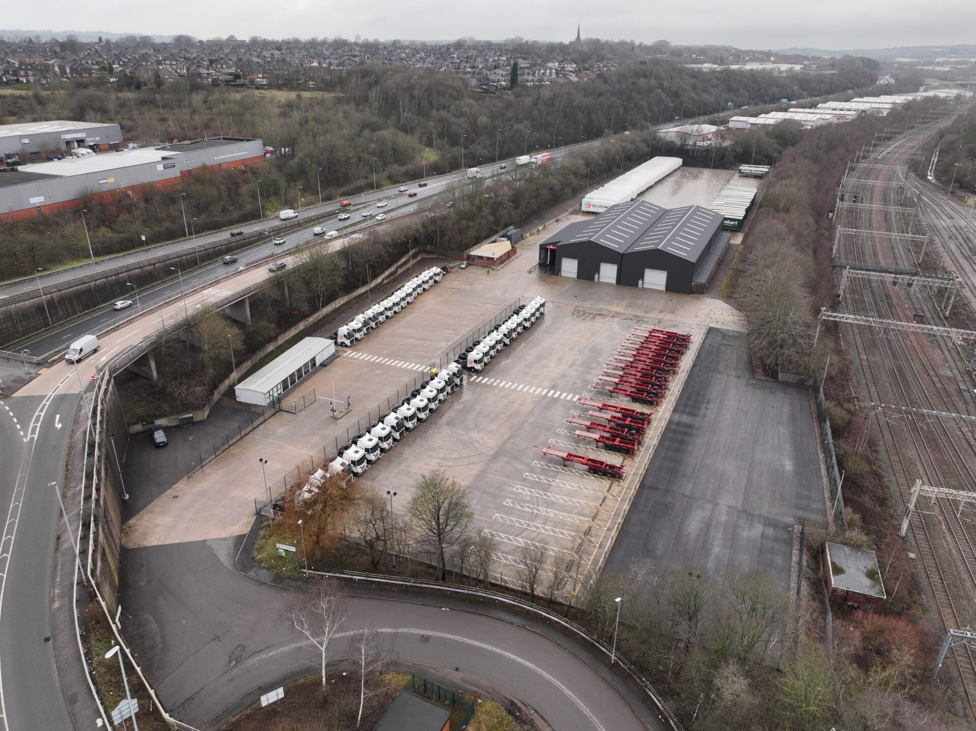 Aerial view of a large concreted area featuring a row of trucks, car parking spaces and an industrial building