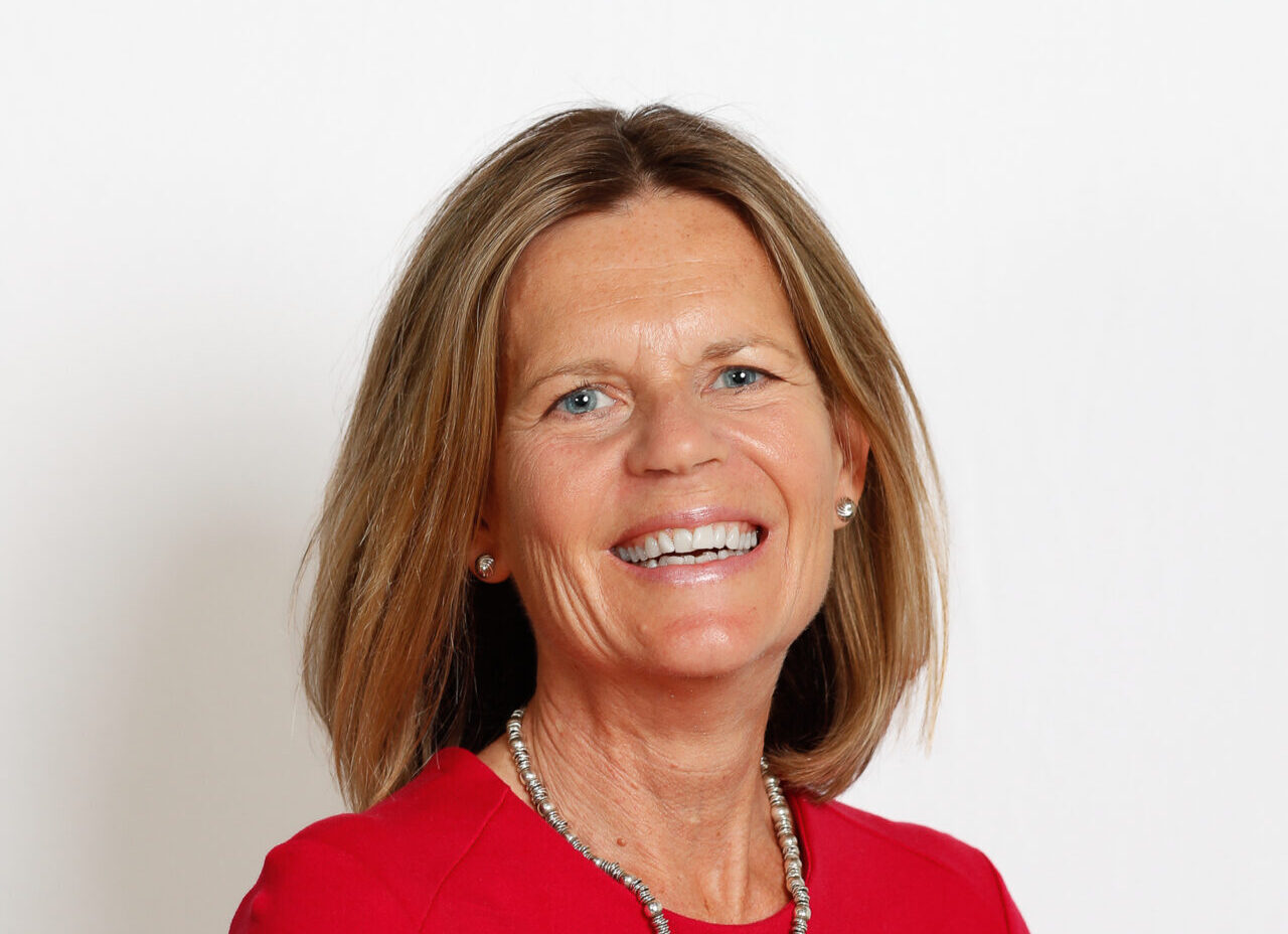 A smiling woman with long brown hair wearing a red dress