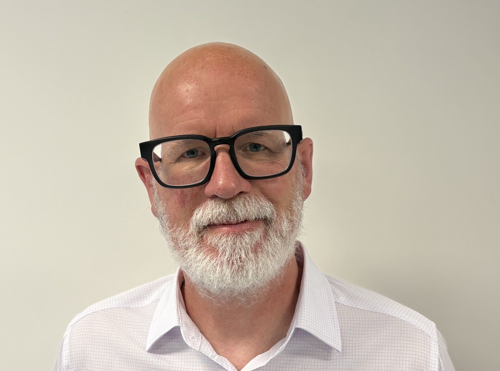 A bearded, bald white man wearing black rimmed glasses and a white shirt