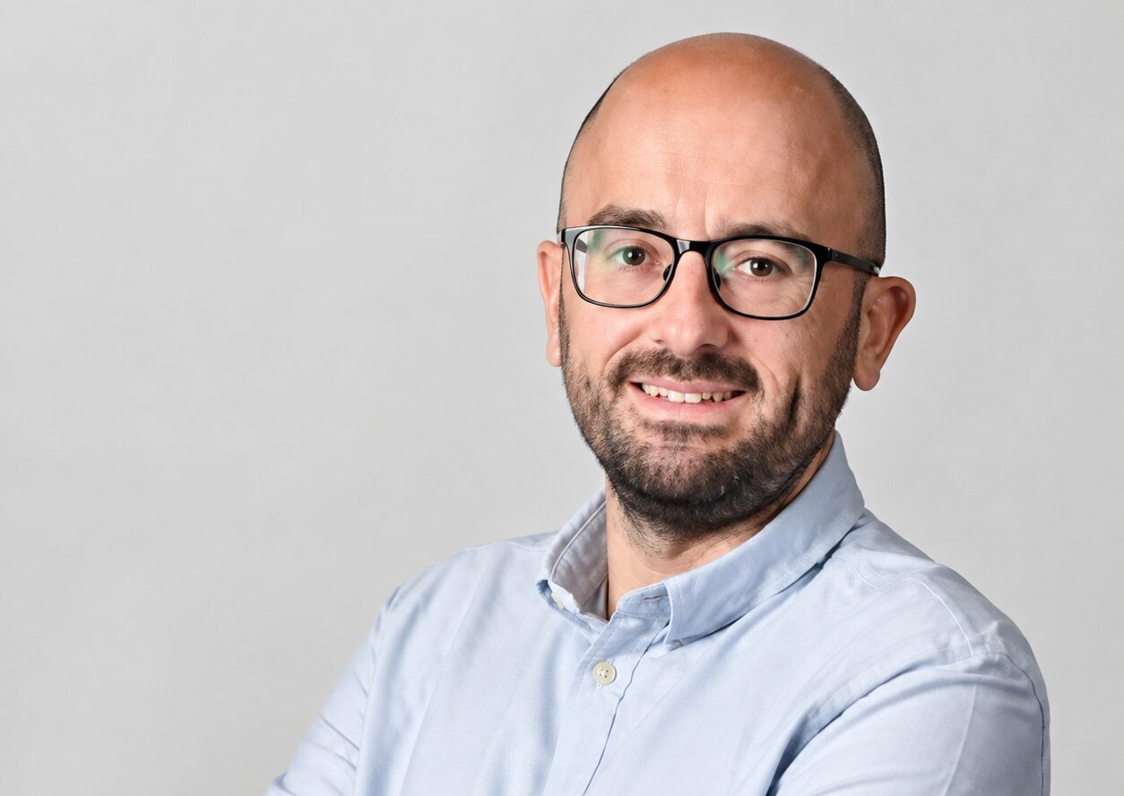 A smiling man wearing glasses and a light coloured shirt
