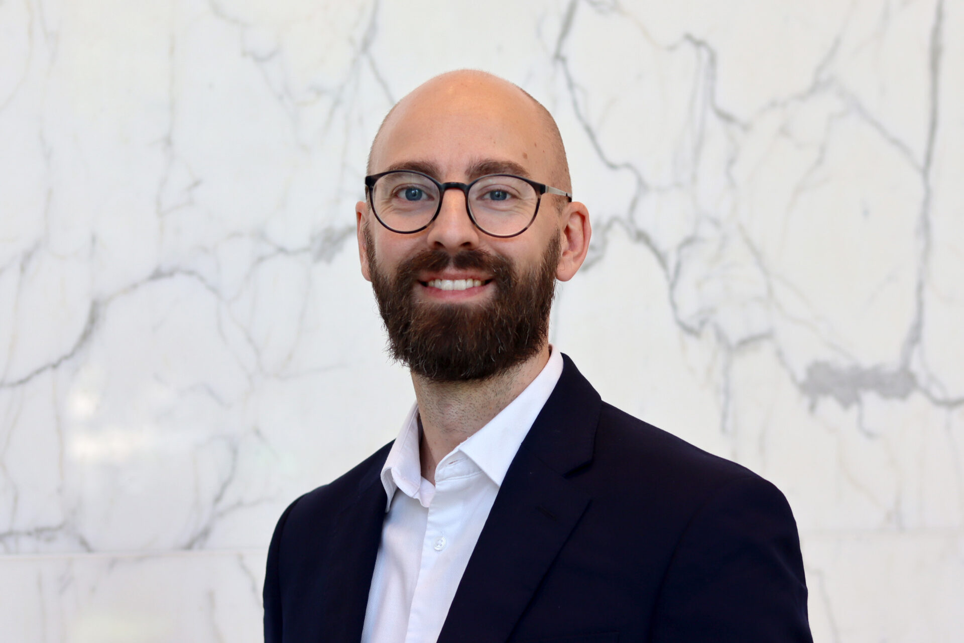 A bald man with a beard wearing a dark suit jacket and a white shirt