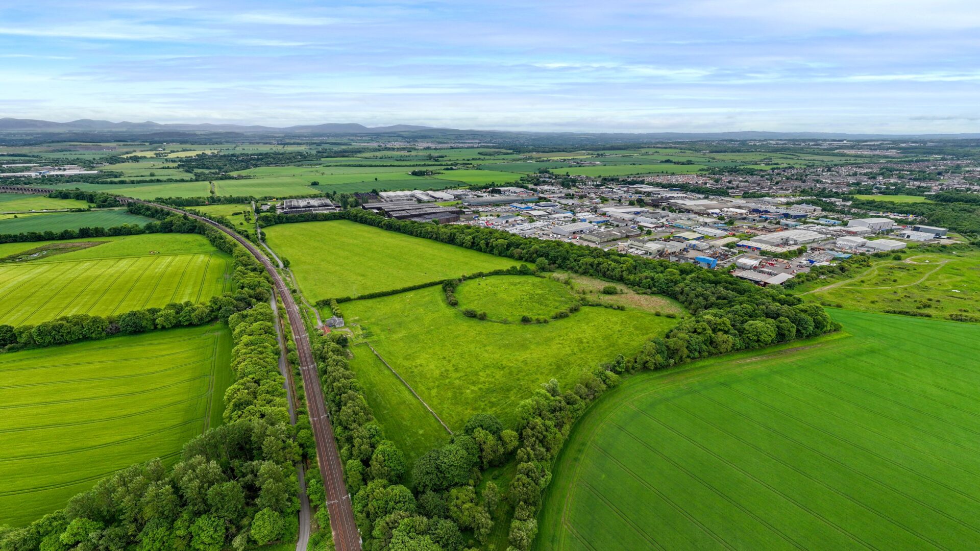 A series of green fields with an industrial estate in the distance