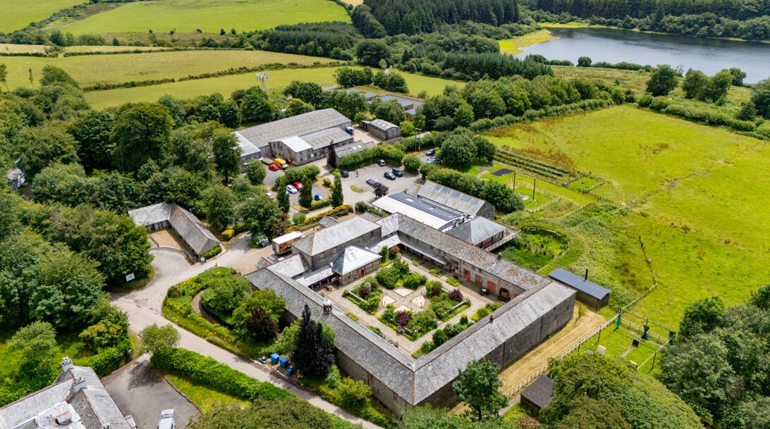 Aerial view of a complex of different buildings surrounded by green fields