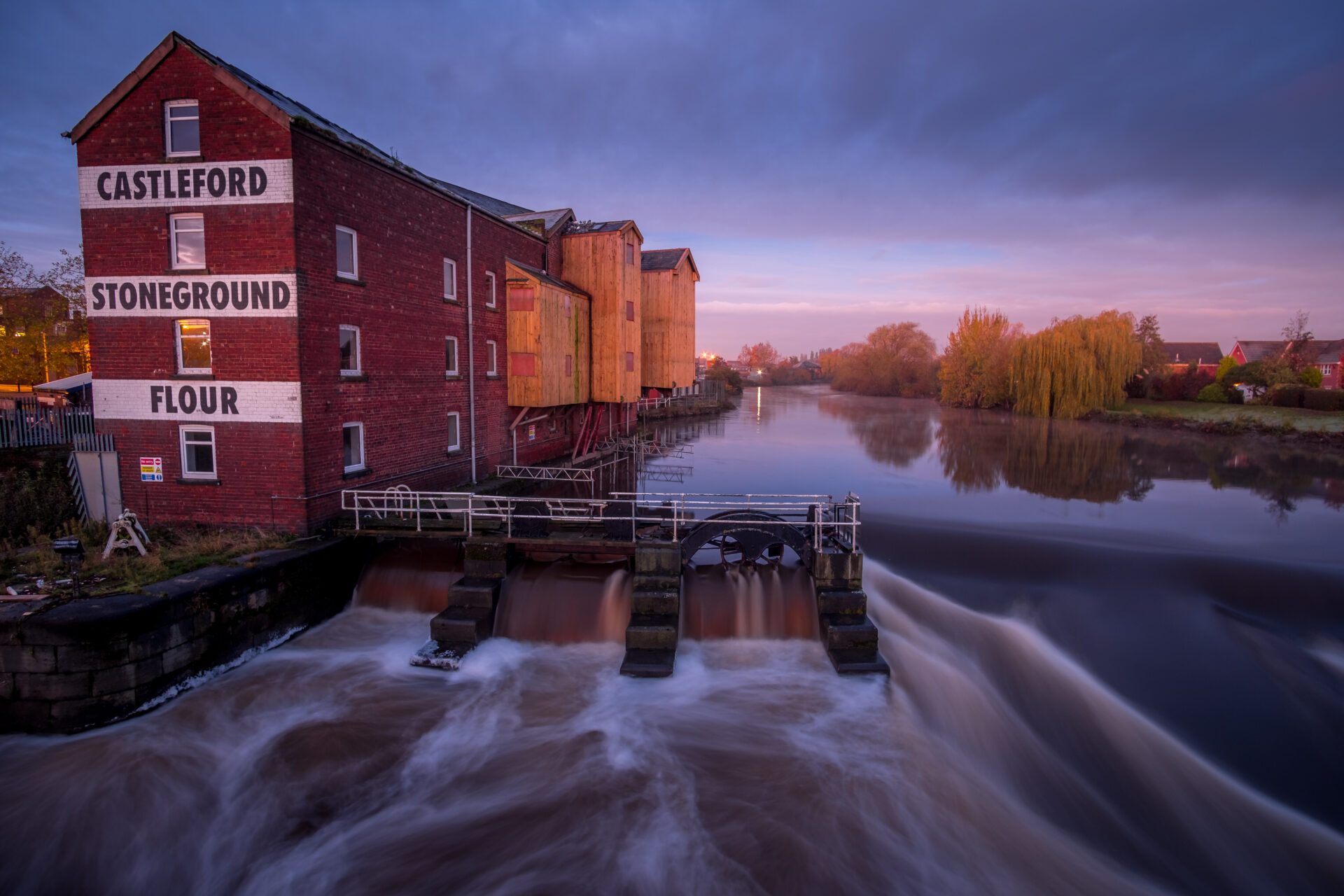 A fast flowing river with a brick built former mill building on the river banks