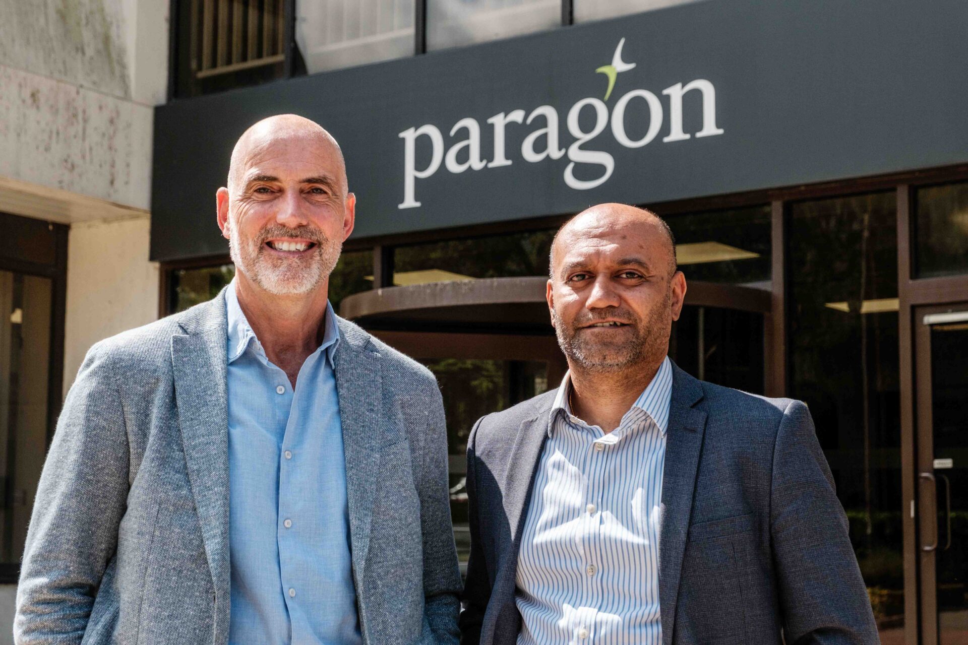 Two men wearing suit jackets and shirts stood infront of a Paragon sign