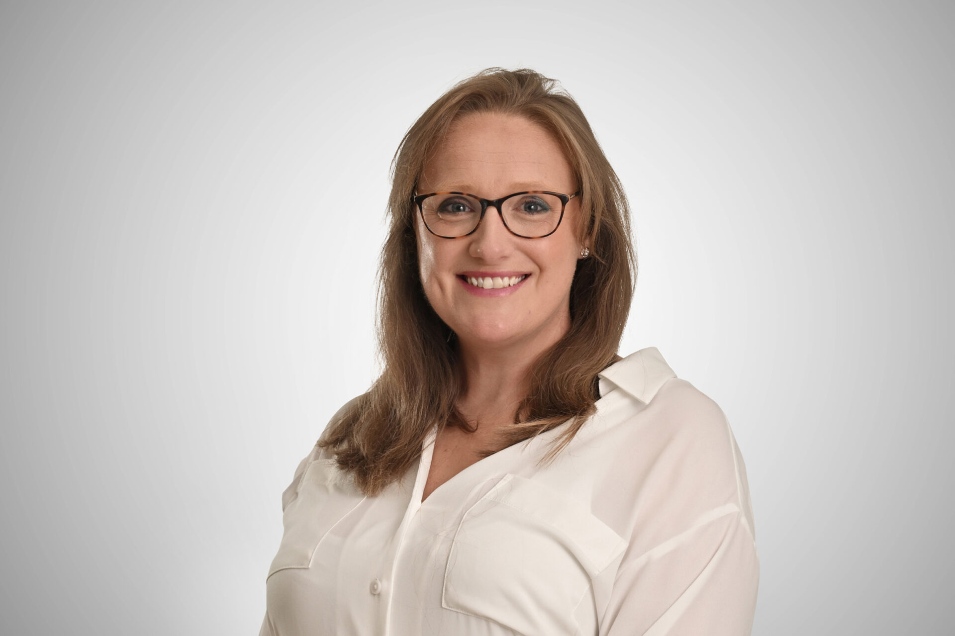 A woman with long brown hair wearing glasses and a white shirt
