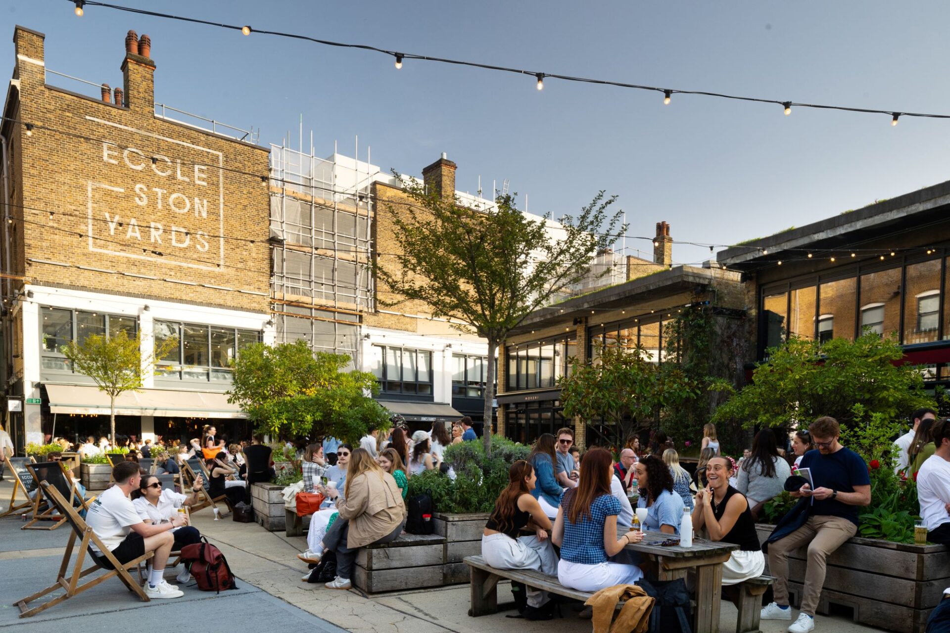 Lots of people sat in a courtyard area on benches and deckchairs