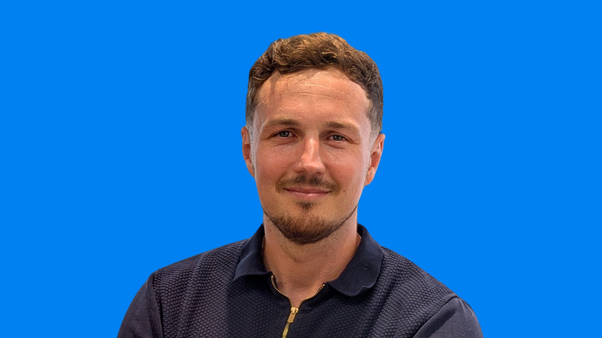 A smiling man with a beard and moustache wearing a dark blue shirt