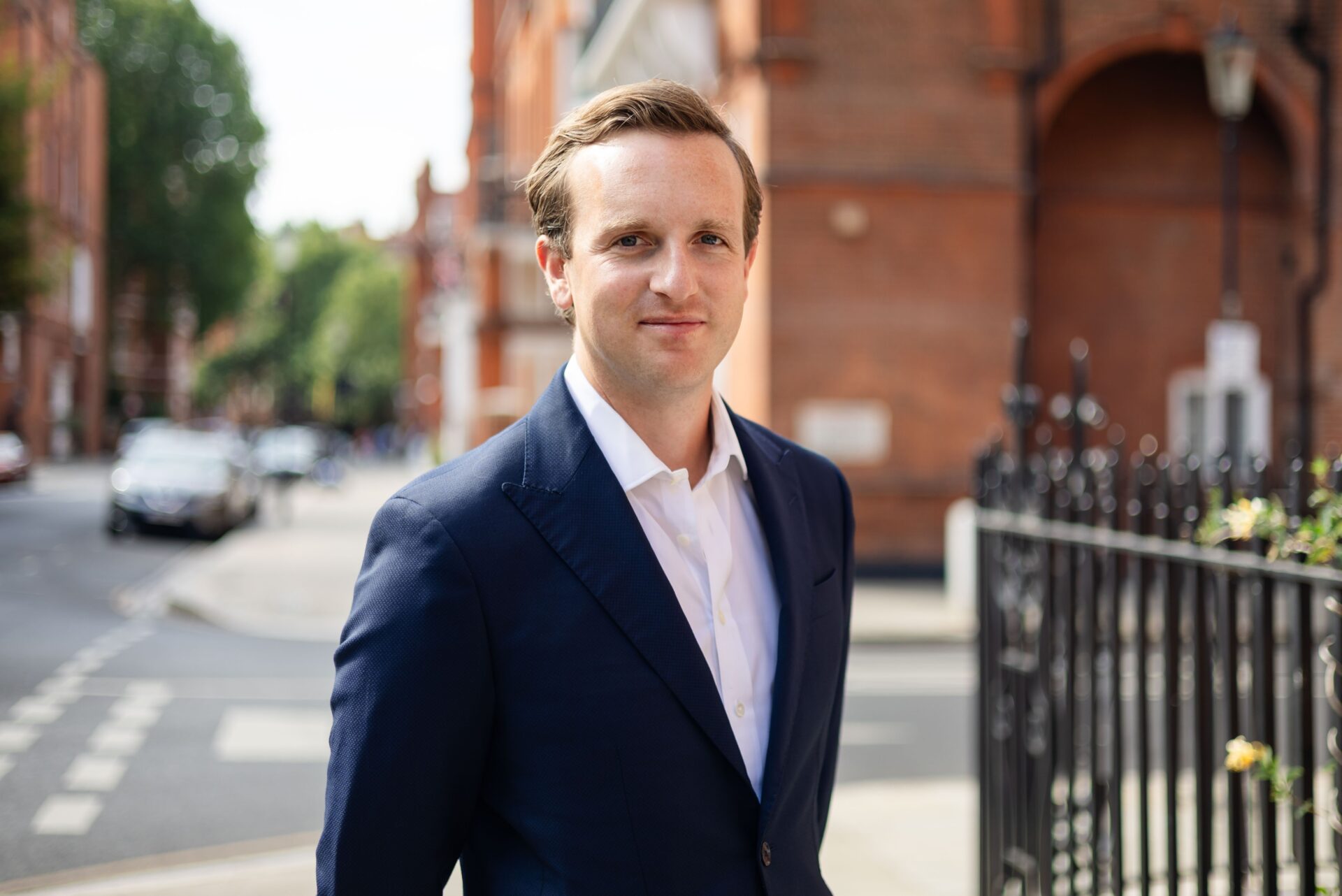 A man on a street corner wearing a dark blue suit jacket and a white shirt