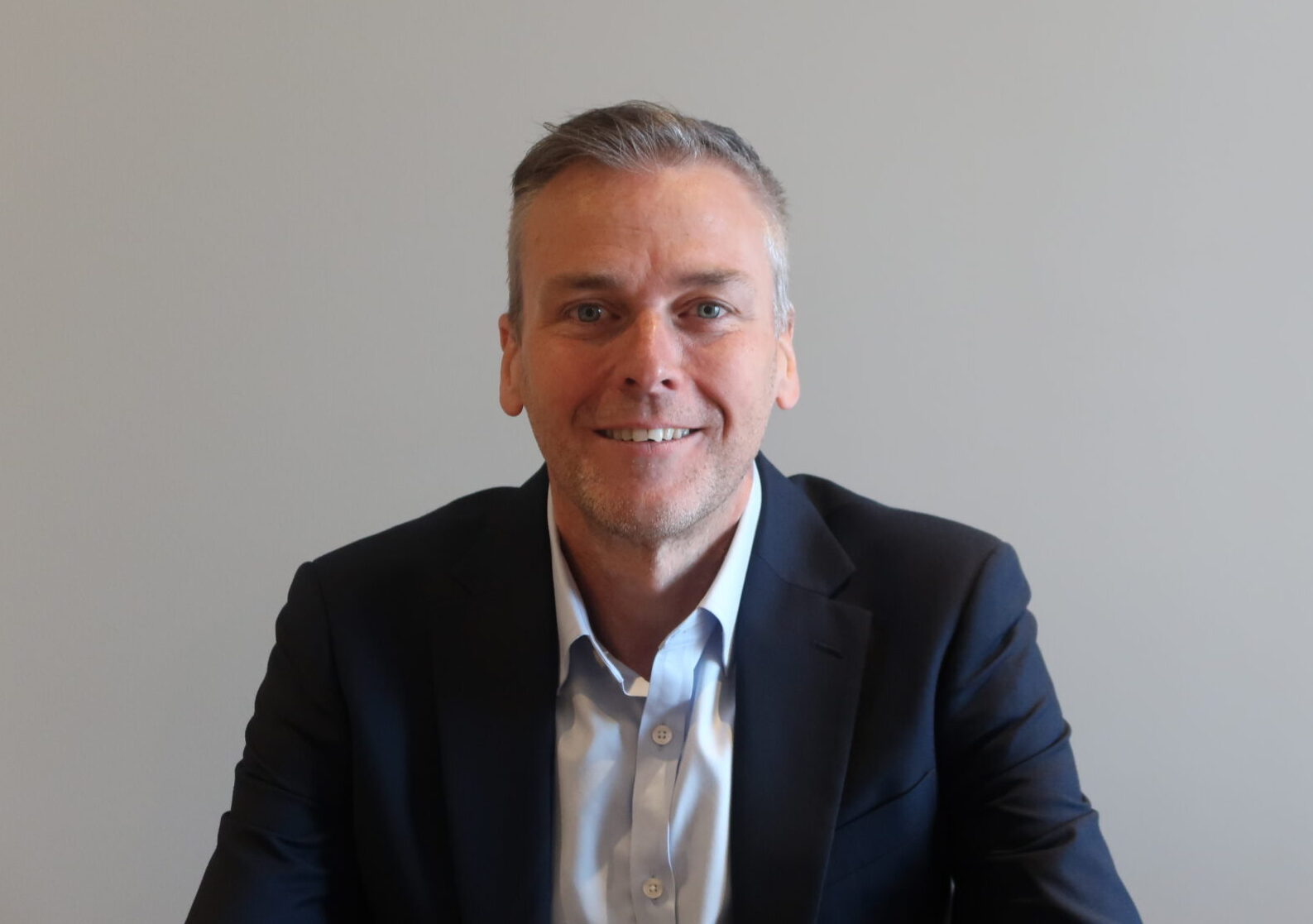 A smiling man wearing a dark suit jacket and a light coloured shirt