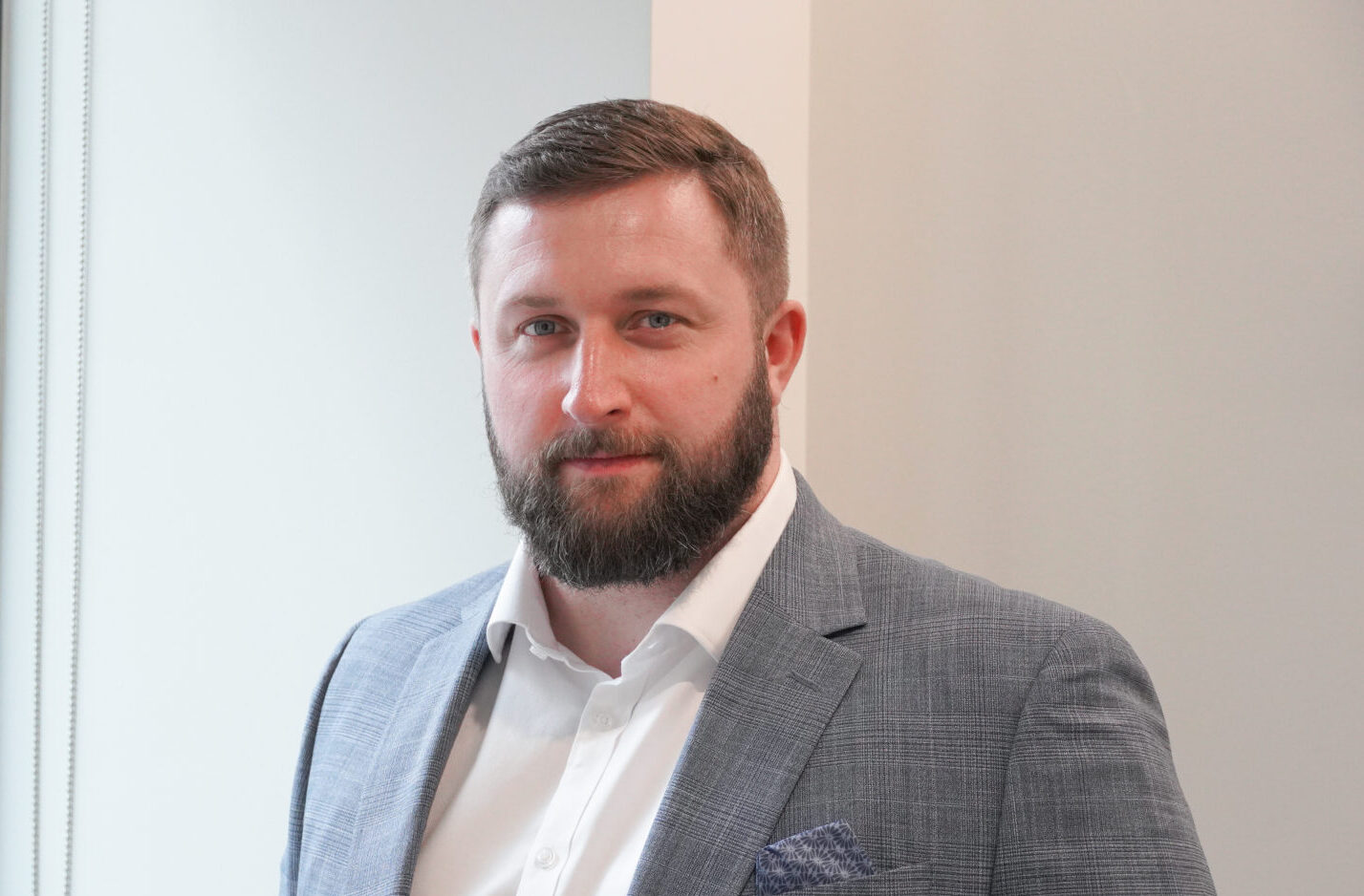 A man with a beard wearing a grey suit jacket and a white shirt