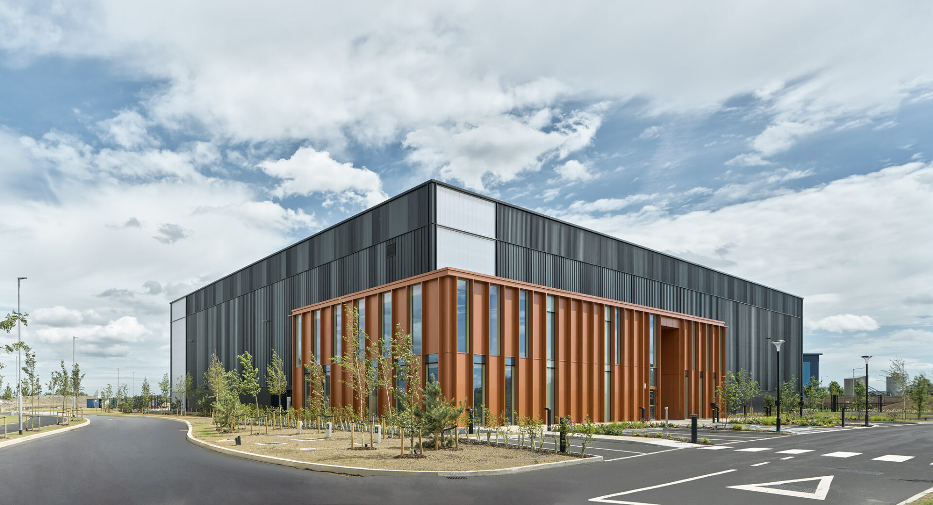 A modern logistics facility with a black and brown facade and car parking in front