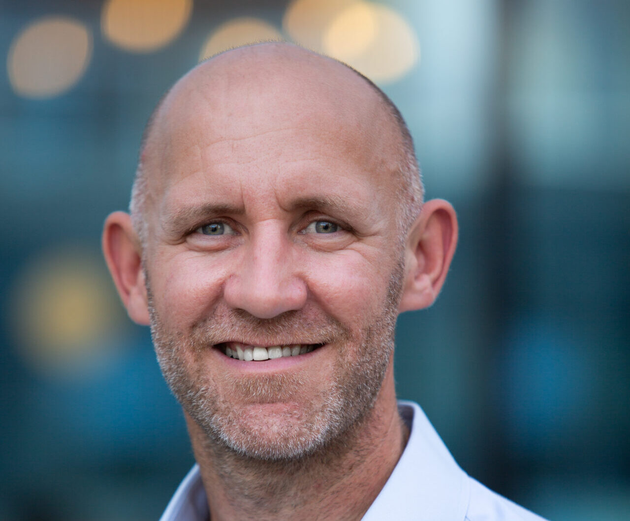 A smiling man wearing a blue collared shirt