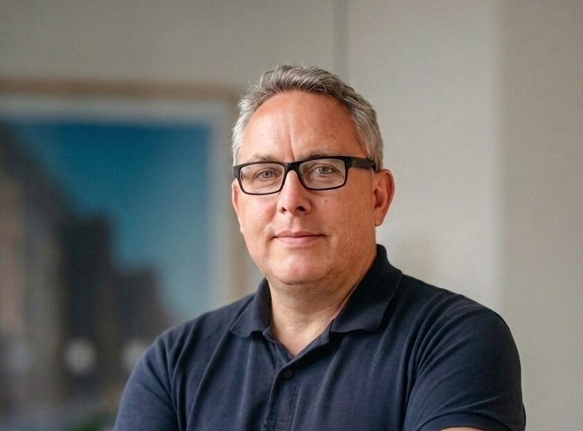 A man with his arms crossed wearing glasses and a dark blue polo shirt