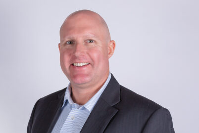 A smiling man wearing a dark suit jacket and a light coloured shirt