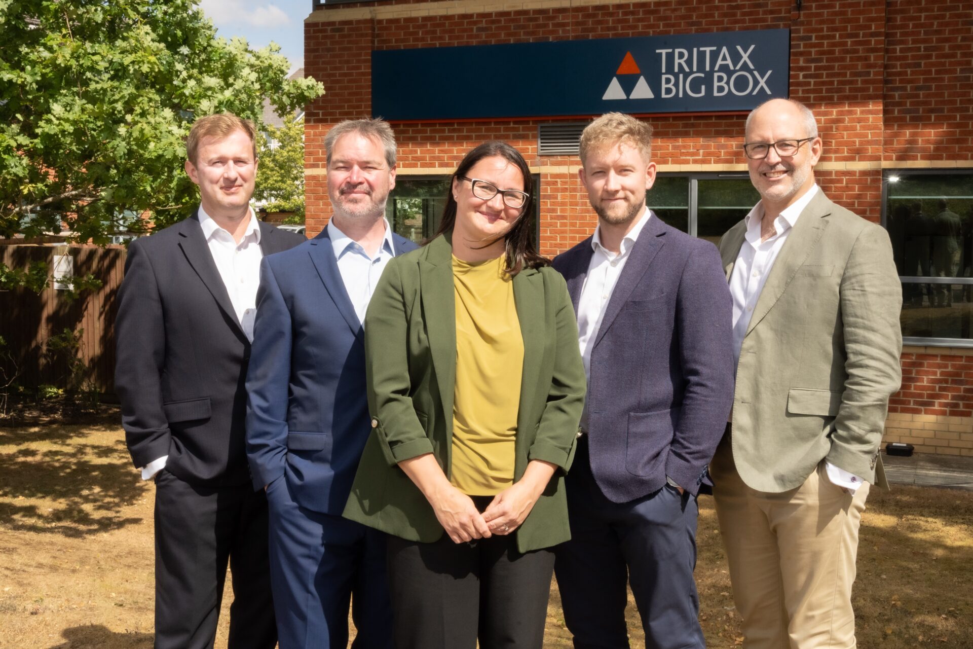 A group of four men and one woman stood in front of a Tritax sign