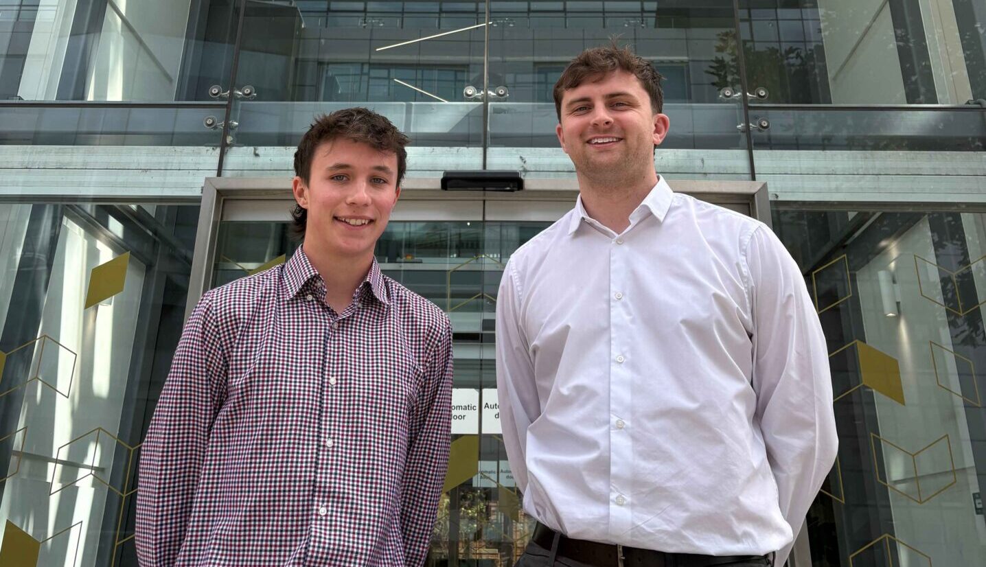 Two men wearing collared shirts standing in front of a glass entranceway